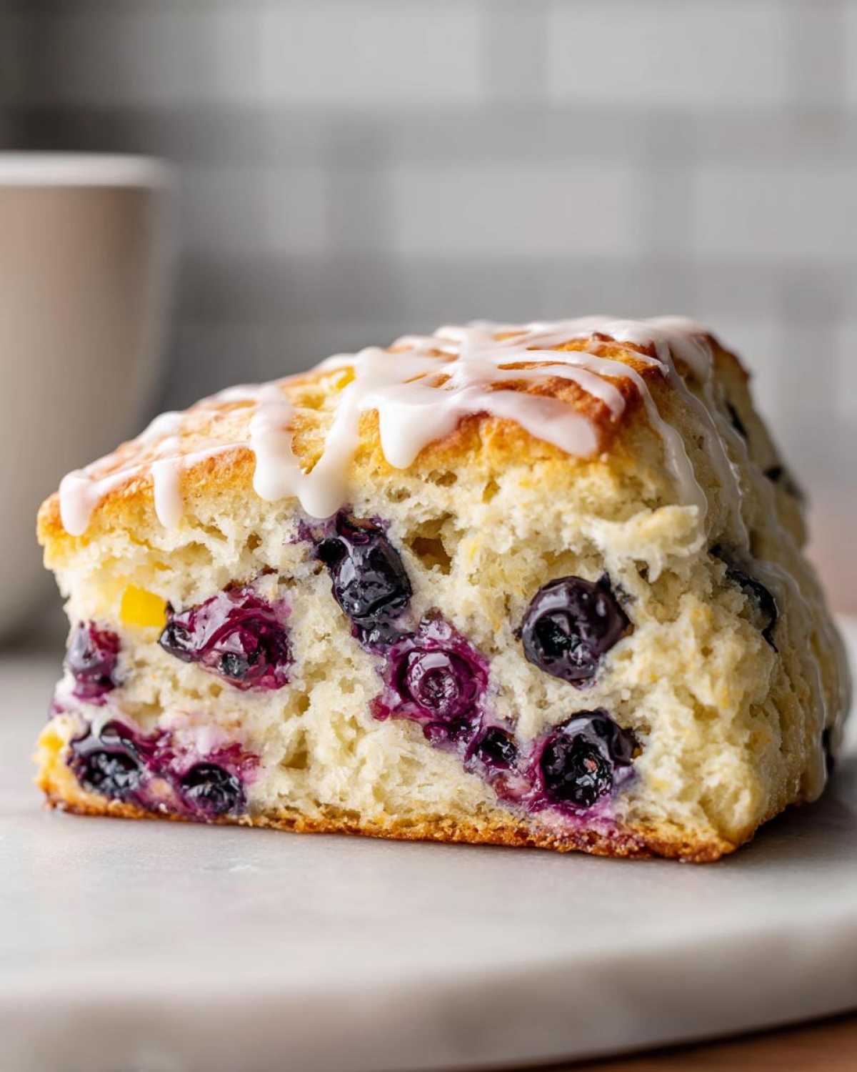A close-up cross-section of a freshly baked blueberry scone, loaded with juicy blueberries and topped with white icing.