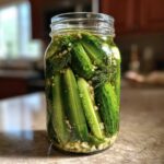 Close-up of fresh cucumbers packed tightly in a glass jar for refrigerator pickles with visible dill and chopped garlic.
