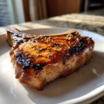 Close-up of a thick, juicy bone-in pork chop cooked to perfection, showing a beautiful caramelized glaze from the marinade for pork chops.