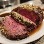 A thick slice of perfectly cooked medium-rare prime rib with a savory herb and garlic crust, resting in au jus.