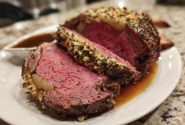 A thick slice of perfectly cooked medium-rare prime rib with a savory herb and garlic crust, resting in au jus.