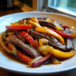 Close-up of juicy steak fajitas strips mixed with vibrant red, yellow, and green bell peppers and onions in a savory sauce.