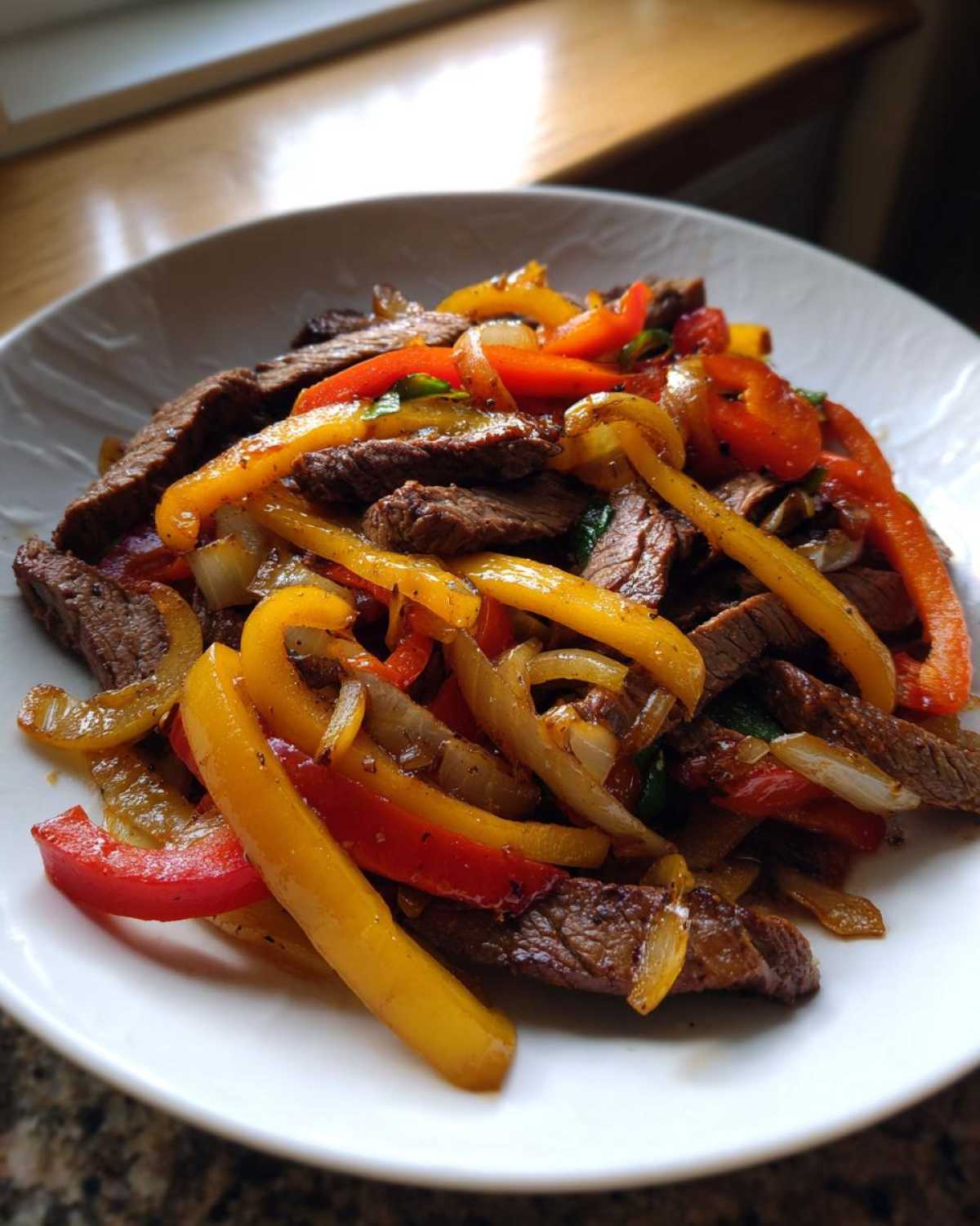 Close-up of a white bowl filled with juicy steak fajitas, featuring sliced beef mixed with vibrant red and yellow bell peppers and onions.