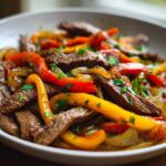 Close-up of juicy steak fajitas featuring sliced steak, red and yellow peppers, and onions, garnished with parsley.