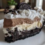 A decadent slice of layered ice cream pie featuring a dark crust, vanilla, chocolate mousse, and whipped topping, garnished with an Oreo.