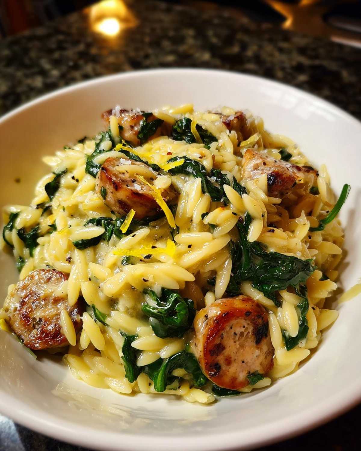Close-up of creamy orzo pasta mixed with spinach, sliced sausage, and lemon zest.