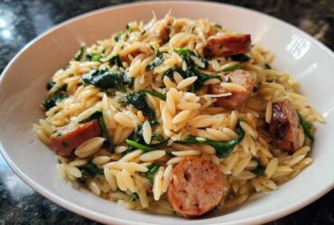 Close-up of a white bowl filled with creamy Lemon Garlic Parmesan orzo pasta mixed with spinach and sliced sausage.