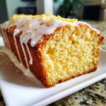 Close-up of a slice of moist lemon pound cake drizzled with white icing and topped with zest.