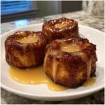 Three golden brown baked apple fritters topped with a thick caramel glaze, served on a white plate.