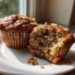 Two delicious banana nut muffins on a white plate, one broken open to show the moist interior.