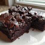 Close-up of three fudgy black bean brownies topped with melted chocolate chips on a white plate.