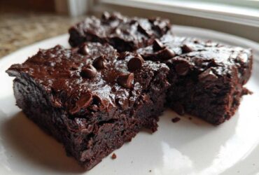 Close-up of three fudgy black bean brownies topped with melted chocolate chips on a white plate.