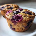 Close-up of a freshly baked blueberry protein muffins showing a moist, golden crumb and burst berries on top.