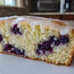 Close-up of a moist slice of blueberry scones, showing rich purple berries and a sweet vanilla glaze topping.