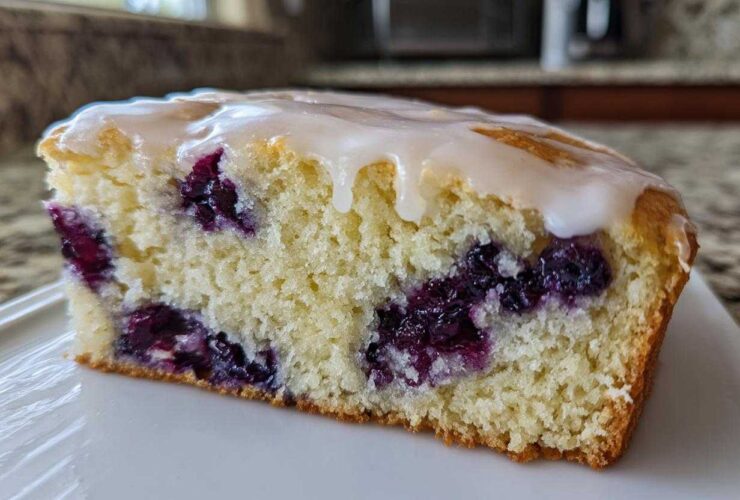 Close-up of a moist slice of blueberry scones, showing rich purple berries and a sweet vanilla glaze topping.