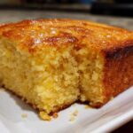 Close-up of a golden, moist slice of buttermilk cornbread with a shiny, slightly caramelized top.
