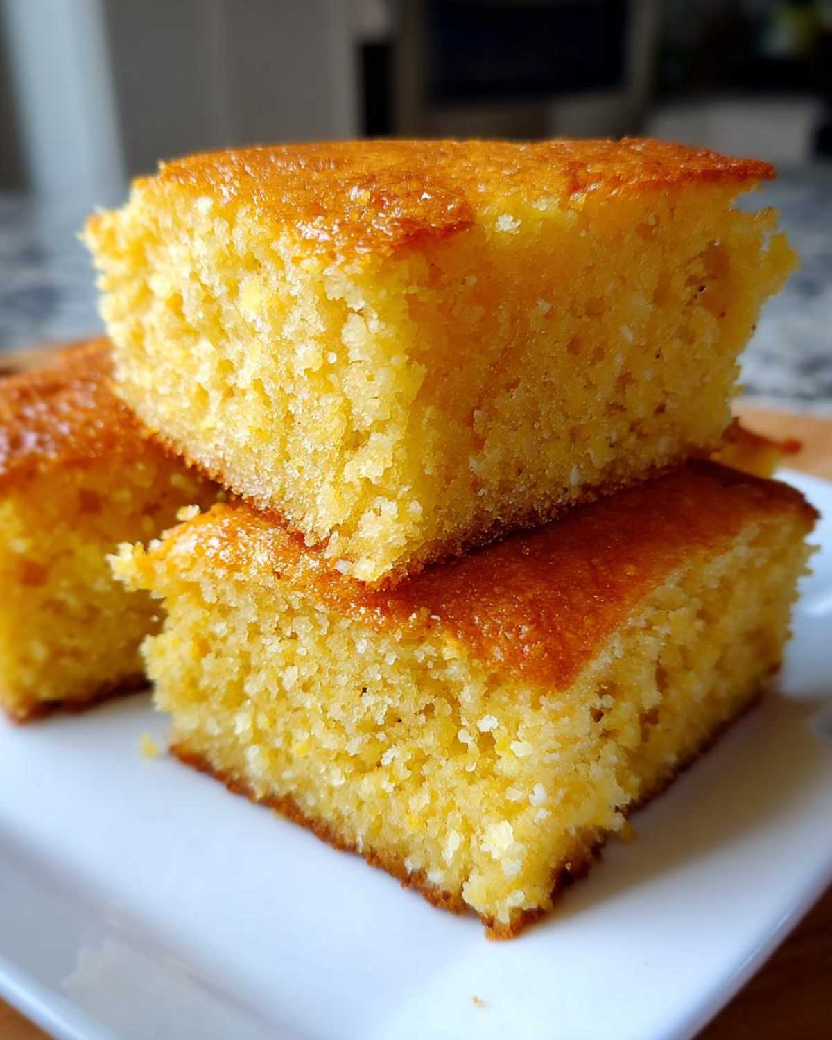 Close-up of three golden, moist slices of buttermilk cornbread stacked on a white plate.