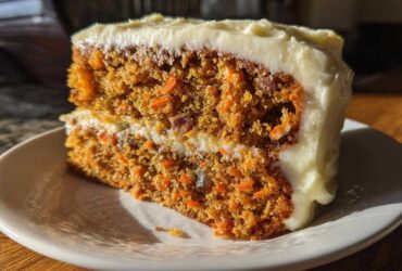 A close-up of a thick slice of moist carrot cake recipe with cream cheese frosting.