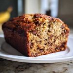 Close-up of a moist slice of chocolate chip banana bread on a white plate.