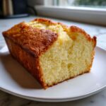 A close-up of a moist, golden-brown slice of condensed milk cake on a white plate.