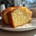 Two thick slices of moist, golden condensed milk cake resting on a white plate, highlighted by sunlight.