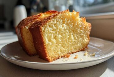 Two thick slices of moist, golden condensed milk cake resting on a white plate, highlighted by sunlight.