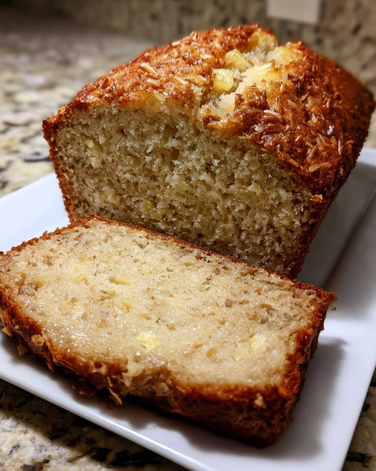 A moist loaf of Hawaiian banana bread, partially sliced, showing a tender crumb and coconut topping.