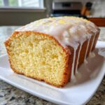 Close-up of a moist lemon loaf drizzled with white glaze and topped with bright lemon zest.