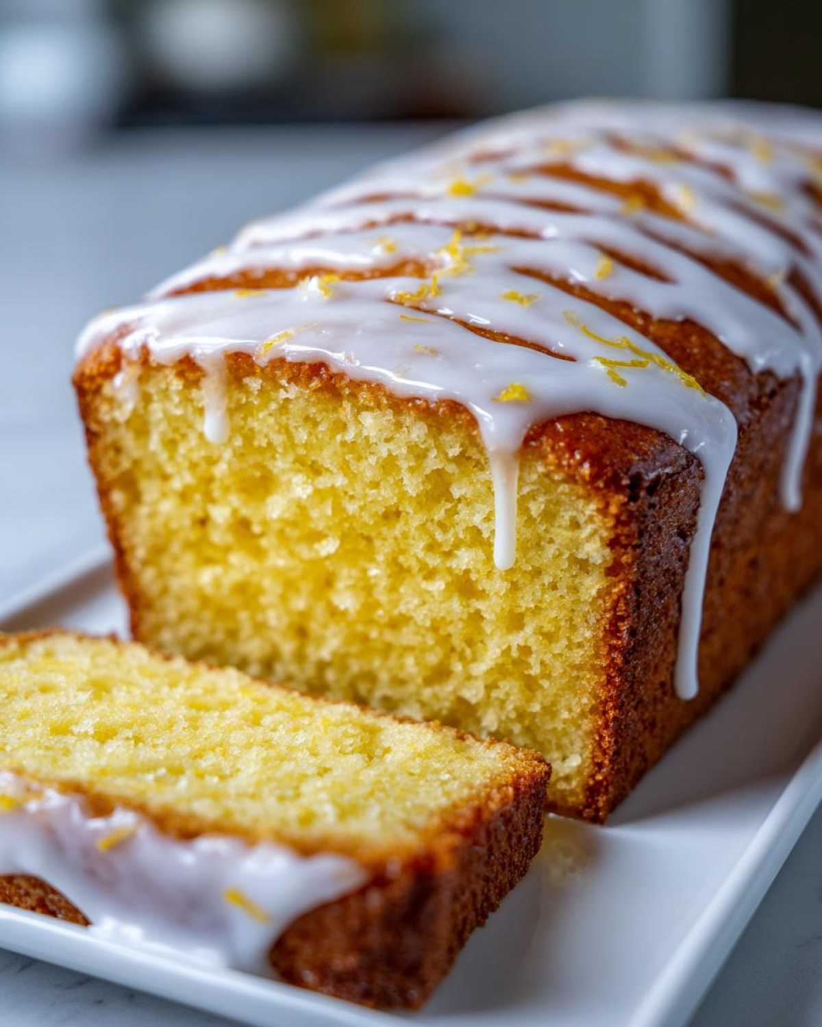 A close-up of a moist lemon pound cake loaf, drizzled with white icing and lemon zest.