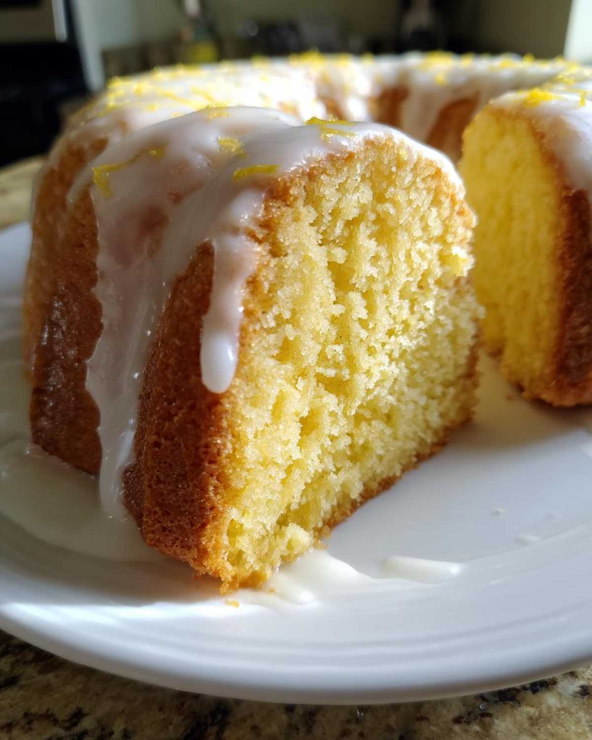 Close-up of a moist slice of lemon pound cake topped with white glaze and lemon zest.