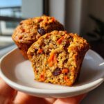 Close-up of a morning glory muffin cut in half showing moist texture, shredded carrots, and raisins inside.