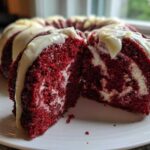 Close-up of a moist red velvet bundt cake slice showing the marbled cream cheese swirl and white glaze.