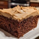 Close-up of a moist slice of dark gingerbread cake topped with thick, light brown frosting.