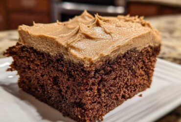 Close-up of a moist slice of dark gingerbread cake topped with thick, light brown frosting.