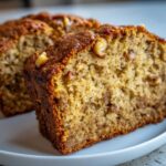 Close-up on a thick slice of moist sugar free banana bread showing a golden-brown crust and visible walnuts.