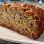 Close-up of a thick, moist slice of sugar free banana bread topped with chopped walnuts on a white plate.