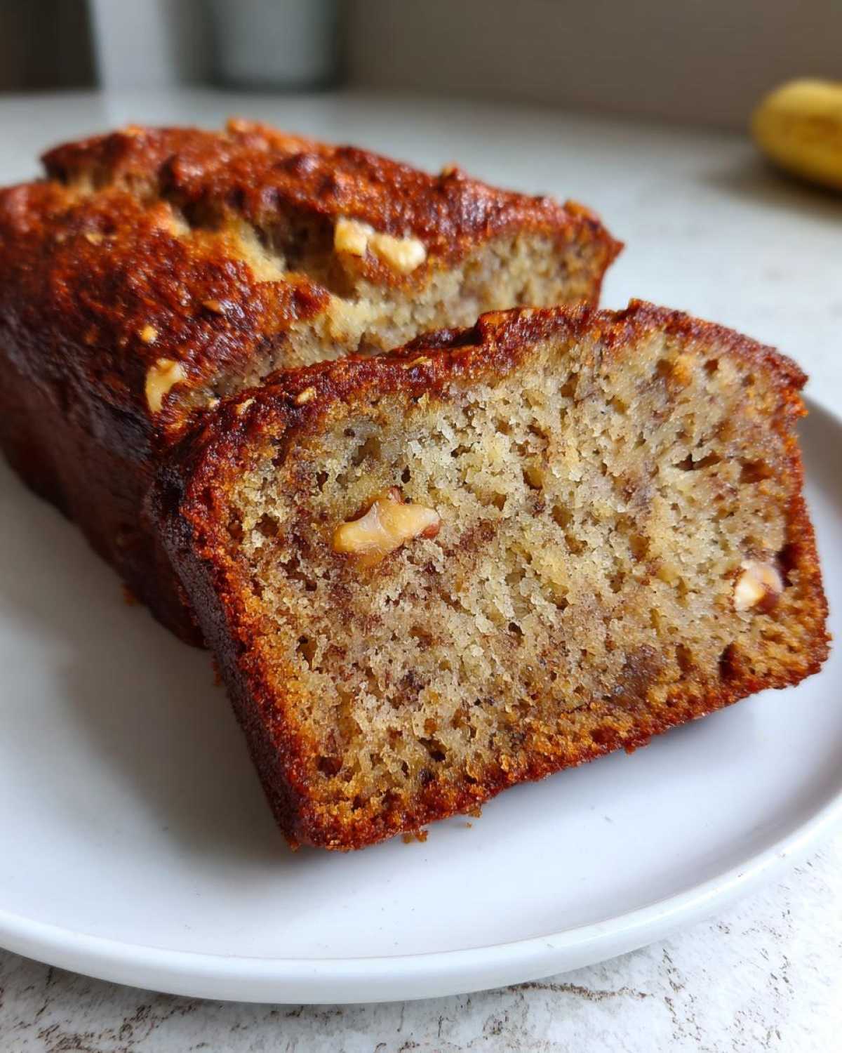 Close-up of a moist slice of sugar free banana bread showing walnuts embedded in the crumb, served on a white plate.