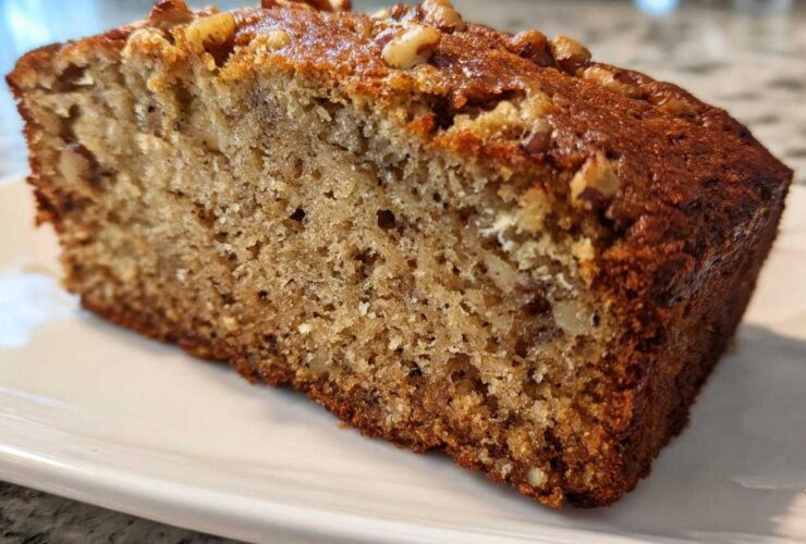 Close-up of a thick, moist slice of sugar free banana bread topped with chopped walnuts on a white plate.