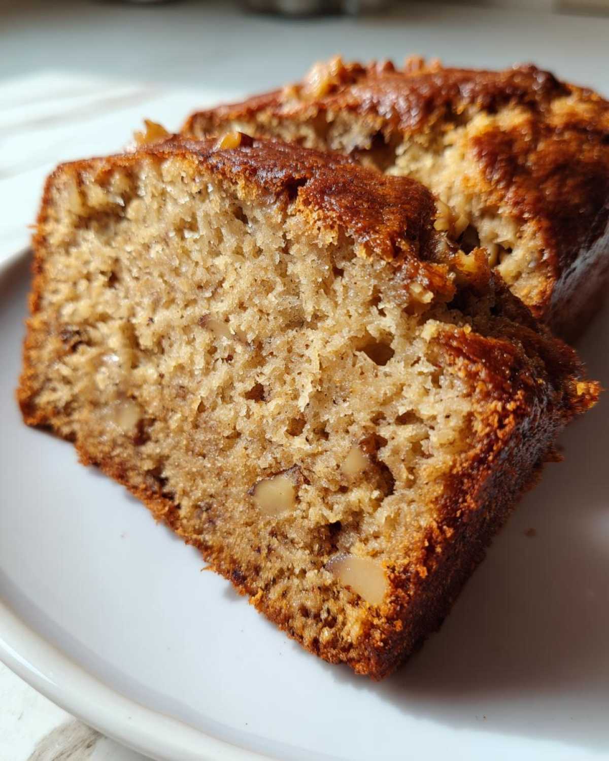 Close-up of two moist slices of sugar free banana bread showing a rich crumb texture and visible walnuts.