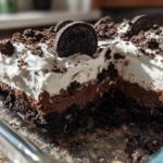 A close-up cross-section of a layered no-bake oreo dirt cake showing cookie crust, chocolate pudding, and whipped topping.