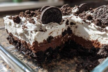 A close-up cross-section of a layered no-bake oreo dirt cake showing cookie crust, chocolate pudding, and whipped topping.