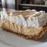 A thick slice of no-bake peanut butter pie showing graham cracker crust, creamy filling, and whipped topping drizzled with peanut butter.
