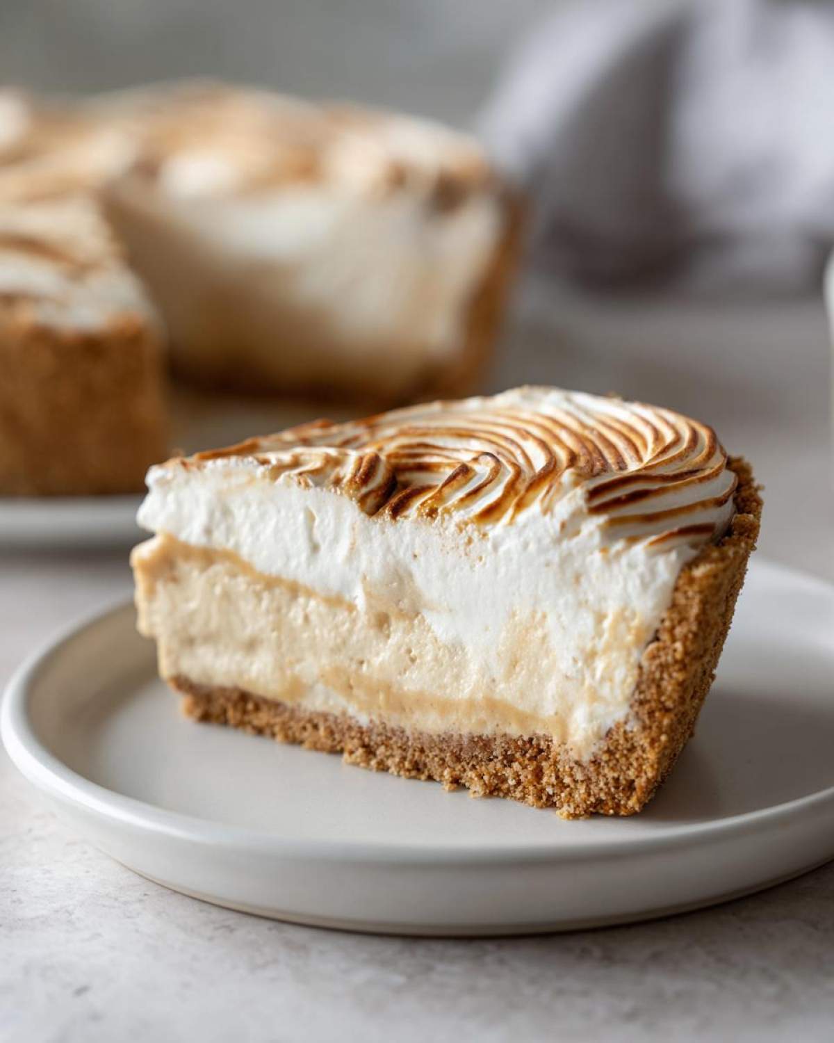 A perfect slice of no-bake peanut butter pie featuring a graham cracker crust, creamy filling, and torched meringue topping.
