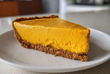 A thick, bright orange slice of no bake pumpkin pie with a dark graham cracker crust served on a white plate.