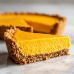 A close-up slice of vibrant orange no bake pumpkin pie showing a thick, creamy filling and a dark graham cracker crust.