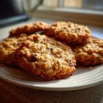 A plate stacked with several golden brown oatmeal breakfast cookie treats, highlighted by natural light.