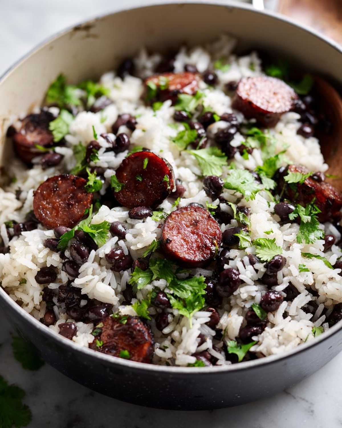 Close-up of one-pot black beans and rice mixed with slices of browned sausage and fresh cilantro.