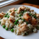 Close-up of a white plate featuring one pot chicken and rice mixed with bright green peas and herbs.