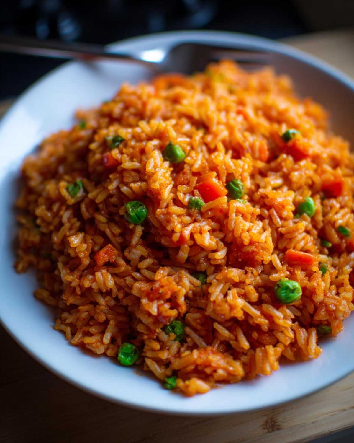 A close-up shot of a white bowl filled with vibrant, orange-red spanish rice mixed with bright green peas and diced carrots.