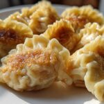 Close-up of several golden-brown, pan-fried Traditional Chinese Dumplings arranged on a white plate.